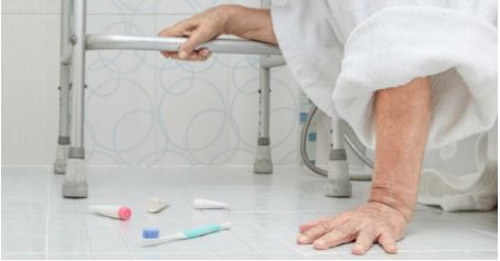 Senior person on bathroom floor reaching for support rail after falling, with toiletries scattered.