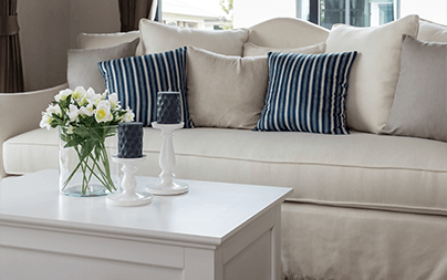 Comfortable beige sofa with striped and solid cushions behind a white coffee table with candles and flowers.