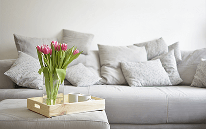 Vase of pink tulips on a wooden tray on a grey couch with multiple cushions.