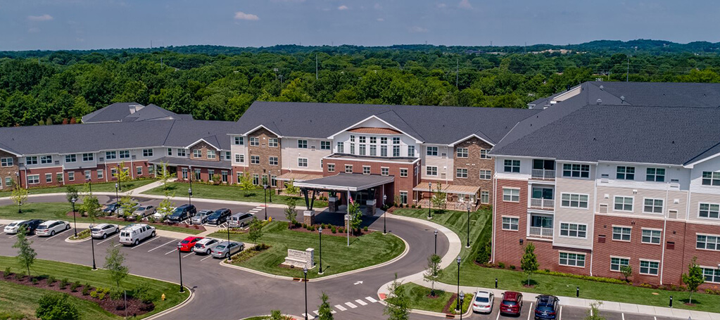 Aerial view of the Clarendale at Indian Lake senior living community surrounded by lush greenery and parked cars.