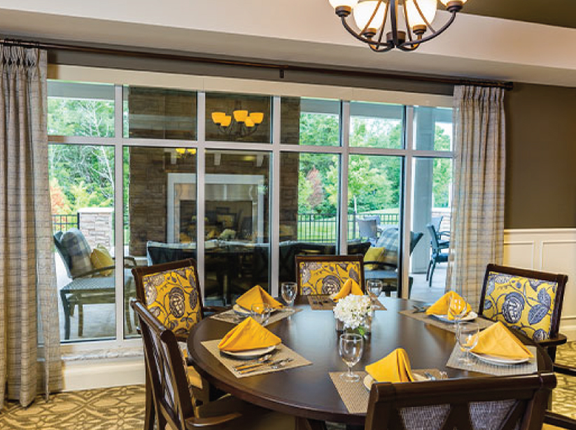Spacious dining room with round table set for six, large windows view to patio, yellow accents.