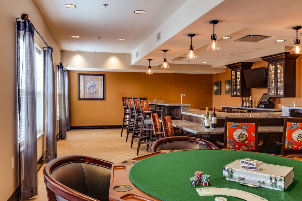 Elegant game room featuring a poker table, bar area with colorful chairs, and modern lighting.