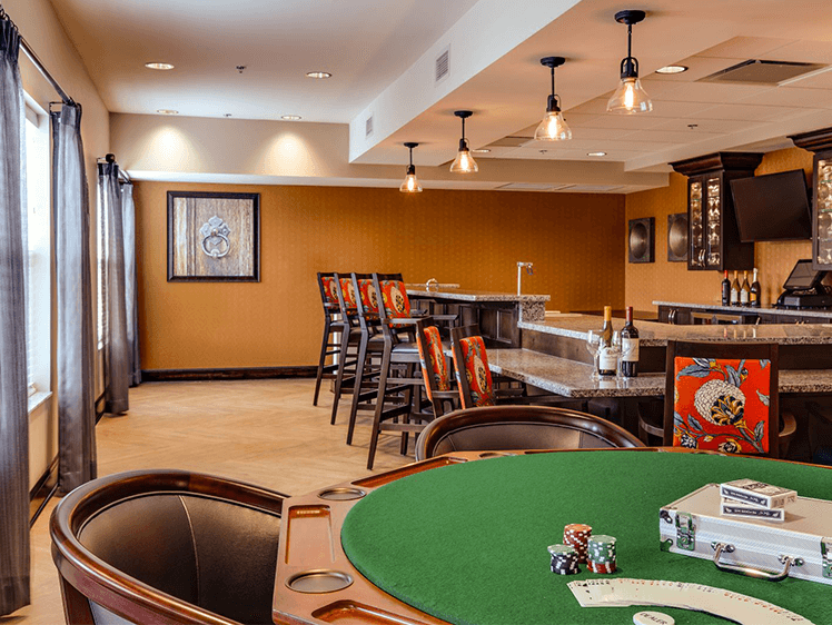 Luxurious game room with poker table, bar seating, modern lighting, and warm decor.