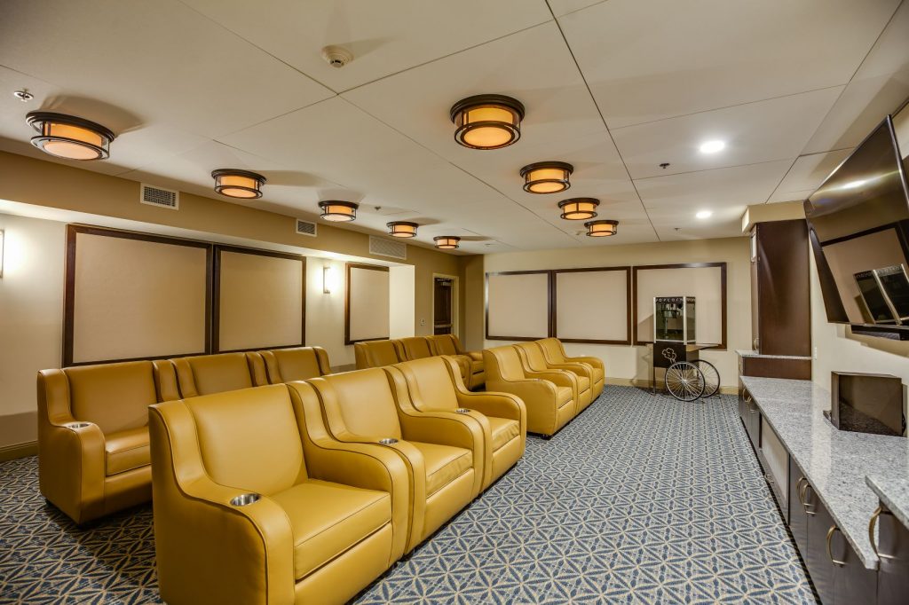 Modern theater room with yellow leather seats, wall-mounted TV, and elegant ceiling lights.