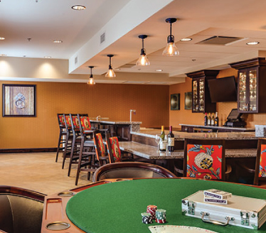 A spacious bar area with a poker table, high chairs, and modern hanging lights.