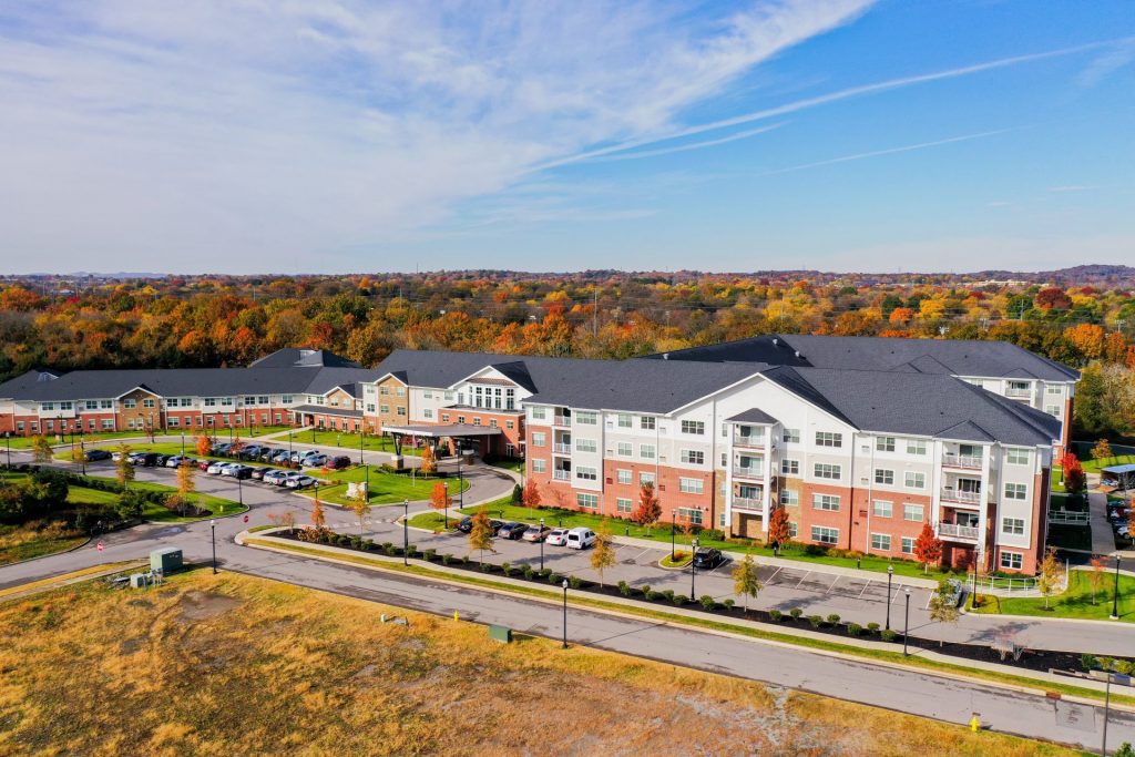Aerial view of a large residential building complex surrounded by autumn foliage and parked cars.