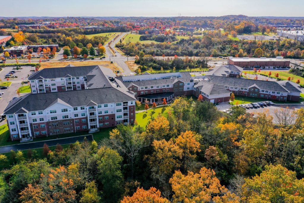 Aerial view of a large residential complex surrounded by colorful autumn trees and open space.